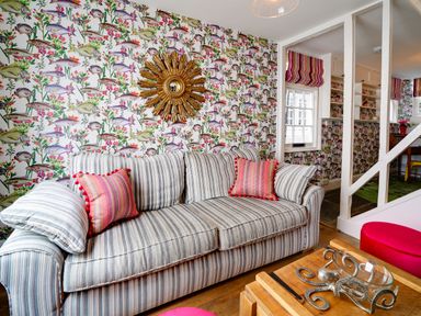 A living room with a striped sofa, fish patterned wallpaper, a golden sunburst mirror, and a wooden coffee table with an octopus decoration at Grey Roofs in Port Isaac