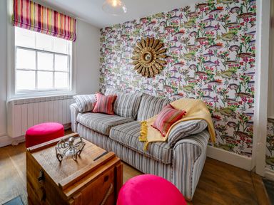 A sitting area with a striped sofa pink cushions pink stools and a wooden chest table at Grey Roofs in Port Isaac