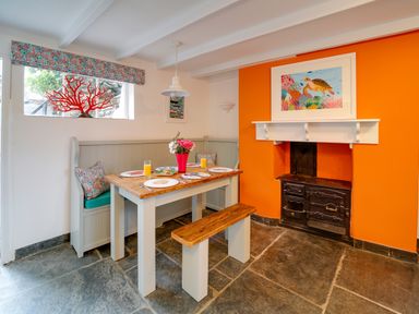 A dining area with table, bench, corner seating, orange wall with fireplace and turtle artwork at Grey Roofs in Port Isaac