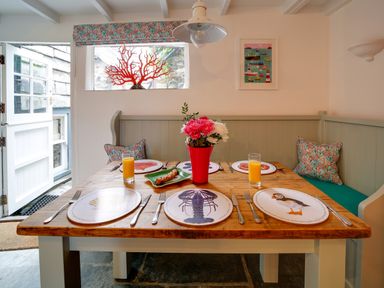 A dining area with a wooden table set with illustrated placemats and glasses of orange juice at Grey Roofs in Port Isaac