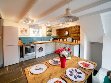 A kitchen with blue tile backsplash wooden countertops and a wooden table with flower vase and decorated plates at Grey Roofs in Port Isaac