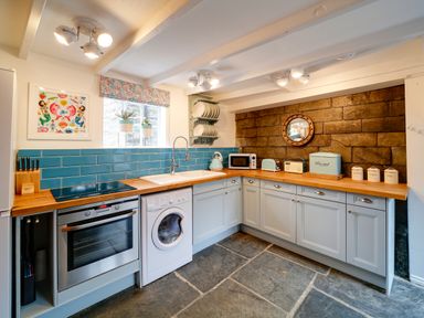 A kitchen with blue tiled backsplash wooden countertops and grey cabinets at Grey Roofs in Port Isaac