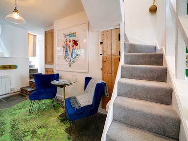A small seating area with two blue chairs and a glass table next to carpeted stairs at Grey Roofs in Port Isaac