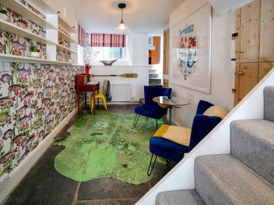 A room with blue chairs a small desk yellow chair patterned wallpaper and green rug at Grey Roofs in Port Isaac