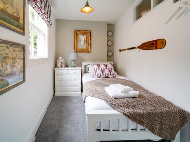 A small bedroom with a single bed a chest of drawers and nautical decorations at Grey Roofs in Port Isaac