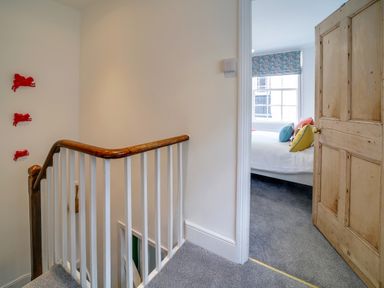 A staircase with white railing and wooden handrail next to a bedroom with colorful pillows on a bed at Grey Roofs in Port Isaac