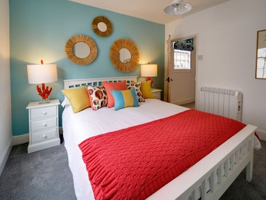 A bedroom with a white bed and red blanket next to two white nightstands with lamps at Grey Roofs in Port Isaac