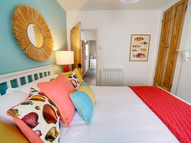 A bedroom with a white bed and colorful pillows with shells and a red runner at Grey Roofs in Port Isaac