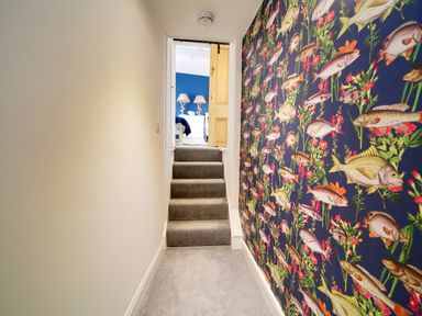 A hallway with carpeted stairs and a wall with fish patterned wallpaper at Grey Roofs in Port Isaac