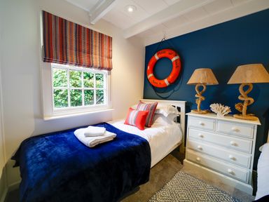 A bedroom with a single bed white dresser with lamps and window with striped blind at Grey Roofs in Port Isaac