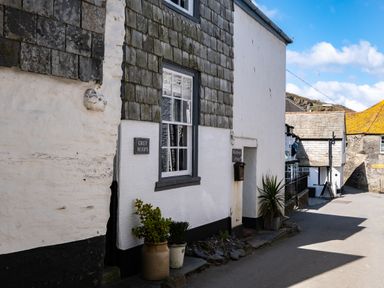 A street view of white and stone cottages with plants in pots outside at Grey Roofs in Port Isaac