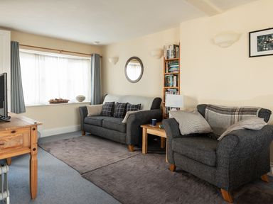 A living room with two grey sofas a wooden table a bookshelf and a window at Sea Glimpses in Port Isaac