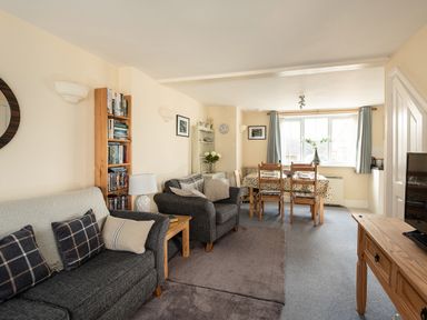 A living room with sofas a wooden dining table and chairs a bookshelf and a television at Sea Glimpses in Port Isaac
