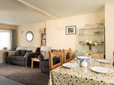 A living room with sofas and a dining table set with plates and glasses at Sea Glimpses in Port Isaac