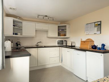 A kitchen with white cabinets a microwave a toaster a kettle and a bread box at Sea Glimpses in Port Isaac