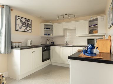 A kitchen with white cabinets blue cups and mugs a kettle and an octopus picture on the wall at Sea Glimpses in Port Isaac