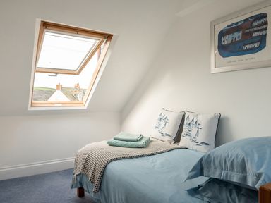 A bedroom with a bed blue bedding and pillows under a slanted ceiling window at Sea Glimpses in Port Isaac