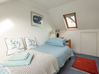 A bedroom with a single bed blue bedding small wooden bedside table with lamp and flowers skylight window and small red rug on blue carpet at Sea Glimpses in Port Isaac