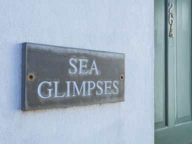 A metal sign reading sea glimpses on a white wall next to a green door at Sea Glimpses in Port Isaac