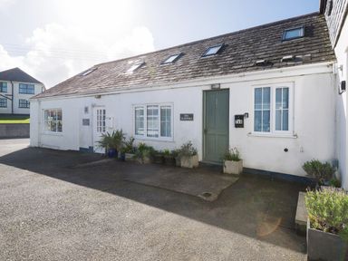 Exterior of a white building with a green door and several windows with potted plants outside at Sea Glimpses in Port Isaac