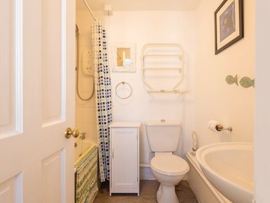 A bathroom with a toilet sink bathtub shower curtain and white cabinet at Sea Glimpses in Port Isaac