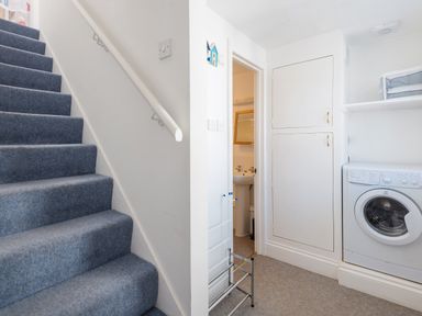 A staircase with blue carpet next to a laundry area with a washing machine and built in white cabinets at Sea Glimpses in Port Isaac