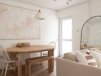 A dining area with a wooden table, chairs, a bench, a hanging light, a large mirror, and a sofa with pillows at Westward 8 Polzeath