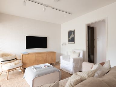 A living room with a sofa armchair ottoman wooden cabinet and a wall mounted television at Westward 8 in Polzeath