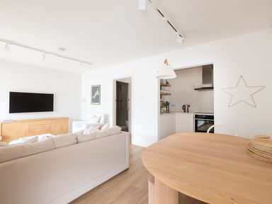 A living room with a beige sofa a wooden sideboard a wall-mounted TV and a round wooden dining table with a pendant light at Westward 8 Polzeath