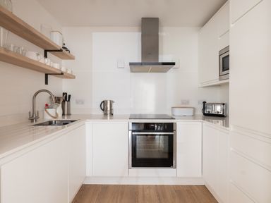 A kitchen with white cabinets stainless steel appliances wooden shelves and a sink at Westward 8 in Polzeath