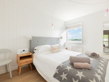 A bedroom with a bed, bedside table, chair, window and towels on a blanket at Westward 8 in Polzeath
