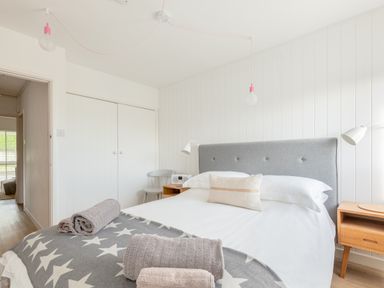 A bedroom with a bed with towels and a star patterned blanket bedside tables lamps and a chair at Westward 8 in Polzeath