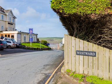 A street with parked cars buildings and a wooden fence with a Westward sign at Westward 8 in Polzeath