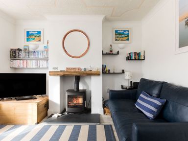 A living room with a wood stove fireplace a blue sofa and shelves with books and DVDs at Number 28 in Port Isaac
