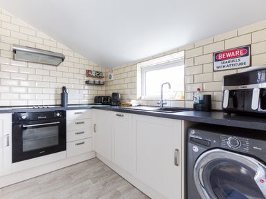A kitchen with white cabinets black countertop an oven washing machine toaster and a window at Number 28 in Port Isaac