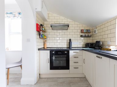 A kitchen with an oven stove black countertop white cabinets and tiled walls at Number 28 in Port Isaac