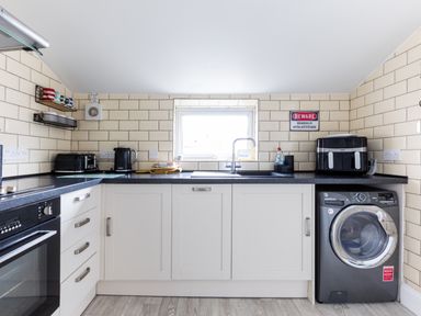 A kitchen with white cabinets black countertop a washing machine toaster kettle and a window at Number 28 in Port Isaac