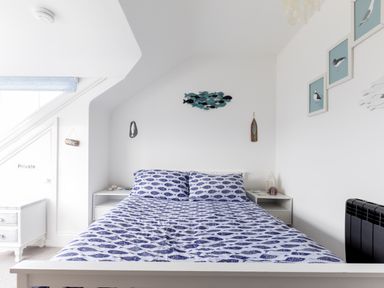 A bedroom with a bed with fish patterned bedding beside two white nightstands and bird artwork on the wall at Number 28 in Port Isaac