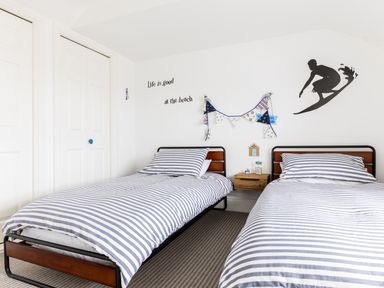 A bedroom with two single beds with striped bedding a wooden nightstand between the beds and wall decorations including a surfer silhouette and text at Number 28 in Port Isaac