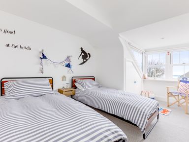 A bedroom with two single beds with striped bedding a wooden chair near a window and a wall decoration with a surfer at Number 28 Port Isaac