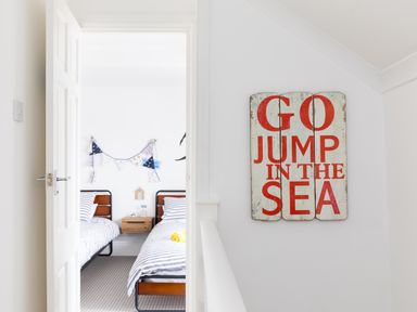 A hallway with a sign that says go jump in the sea and a view into a bedroom with two beds and striped bedding at Number 28 in Port Isaac