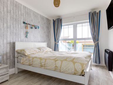 A bedroom with a white bed and beige patterned bedding near a window with blue and white curtains at Number 28 in Port Isaac