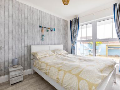 A bedroom with a double bed next to a window with blue patterned curtains and a small nightstand with a lamp at Number 28 Port Isaac