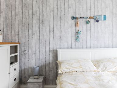 A bedroom with a white bed and beige pillows next to a wooden cabinet and a small wooden table with a lamp on it at Number 28 in Port Isaac