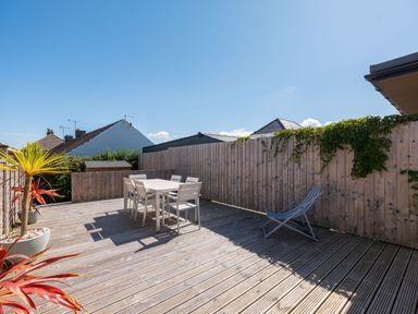 A wooden deck with a dining table and six chairs a folding chair potted plants and a wooden fence at Number 28 in Port Isaac
