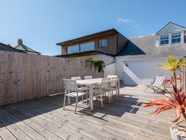 An outdoor wooden deck with a white dining table and six chairs a wooden fence and two potted plants at Number 28 in Port Isaac