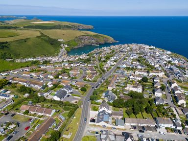 An aerial view of a coastal village with houses a winding road green hills and the ocean in the background at Number 28 in Port Isaac