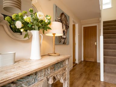 A hallway with a wooden console table holding a white pitcher with flowers and a lamp a wooden door and carpeted stairs at Flaad House in Rock