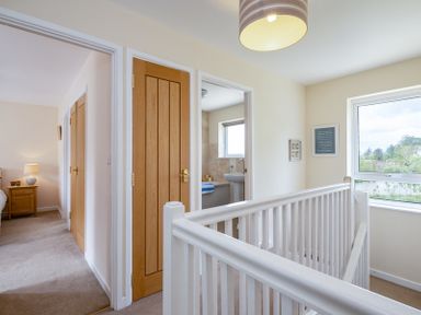 A hallway with white stair railing wooden doors a bedroom and a bathroom window at Flaad House in Rock