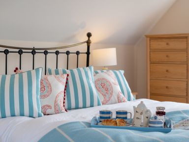 A bedroom with striped and patterned pillows on a bed with a tray holding teacups and pastries at Flaad House in Rock